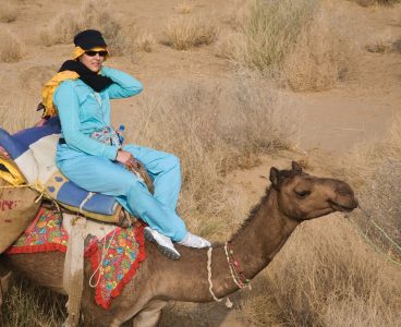 A WOMAN rides a CAMEL in the THAR DESERT during a SAFARI near JAISALMER - RAJASTHAN,