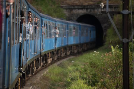 One of the more modern chinese-built blue trains in Sri Lanka photographed with a passanger leaning out.