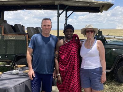 A couple stand with a Masai safari guide in front of a safari vehicle