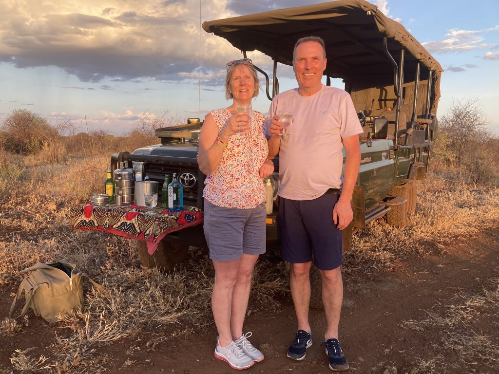 a couple stand holding beverages in front of a 4x4 safari vehicle in a national park in Kenya